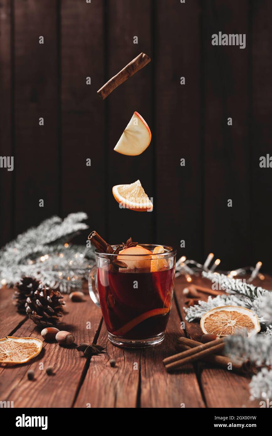 Christmas glass cup or mug with Mulled Wine on wooden table and background with levitating cinnamon stick, dried or sublimated orange, apple slices, a Stock Photo