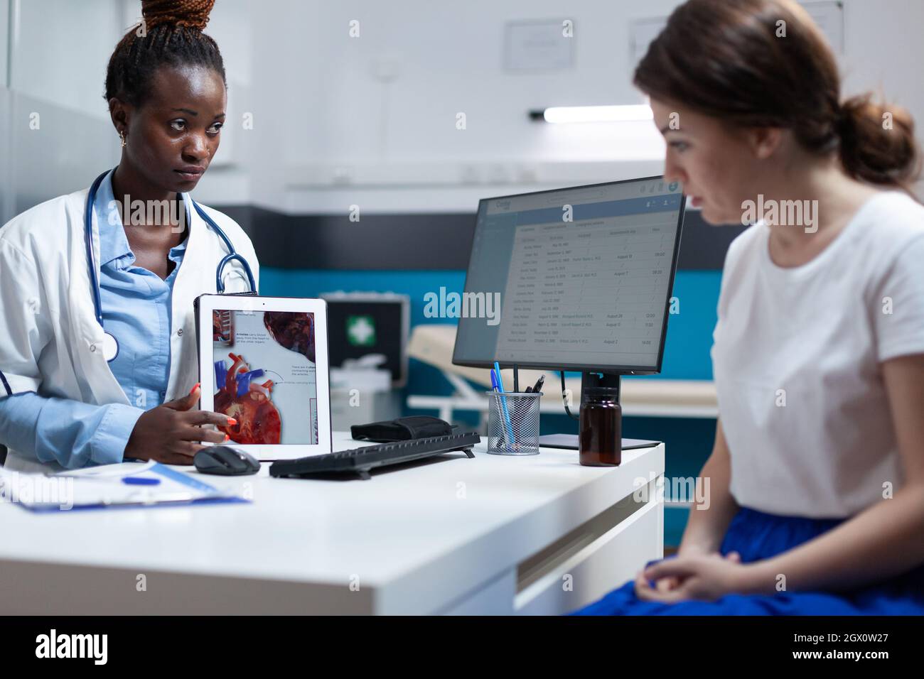 African american cardiologist doctor holding tablet explaining heart xray discussing medical expertise with patient woman during clinical appointment. Radiologist working in hospital office. Stock Photo