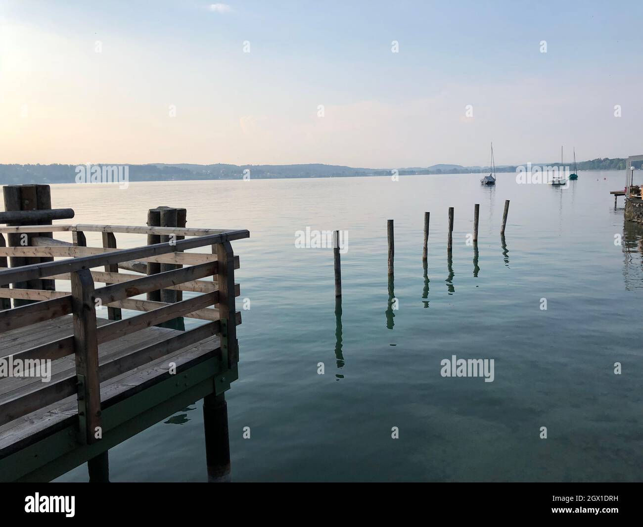 Wooden Posts On Pier Over Lake Against Sky, Southern Munich, Germany. Stock Photo
