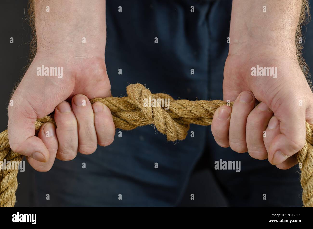 Adult Male tightens the knot on the rope. Hands hold a yellow jute rope