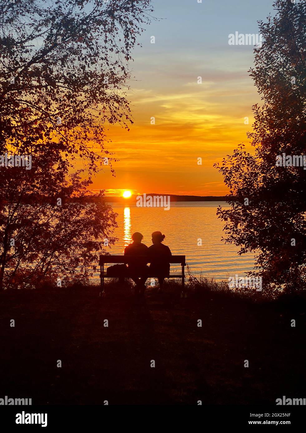 Man and woman sitting on a bench by the lake in beautiful golden summer sunset Stock Photo