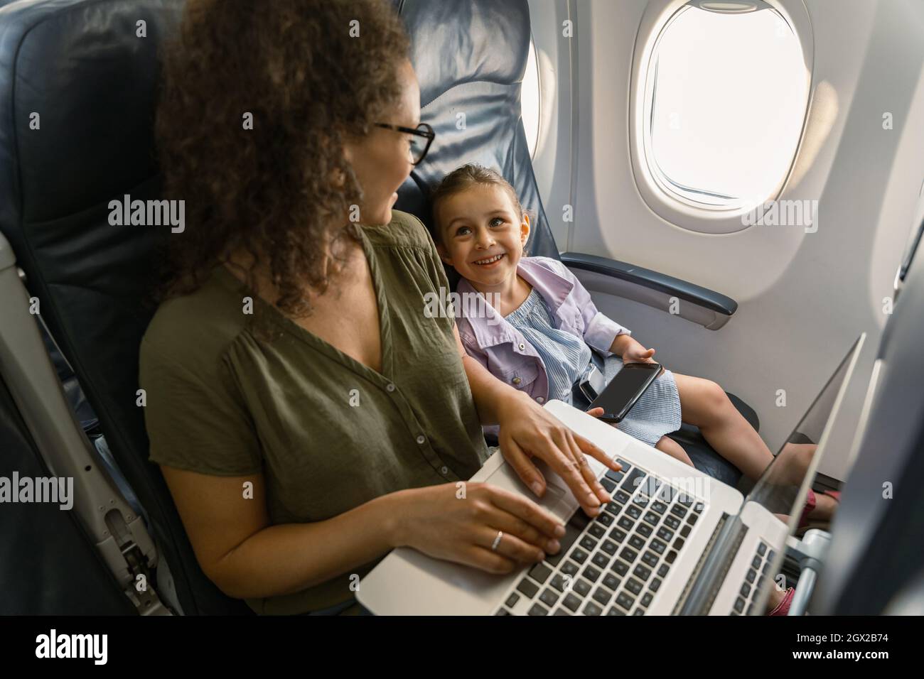 Busy lady working on laptop and looking at her kid while traveling by