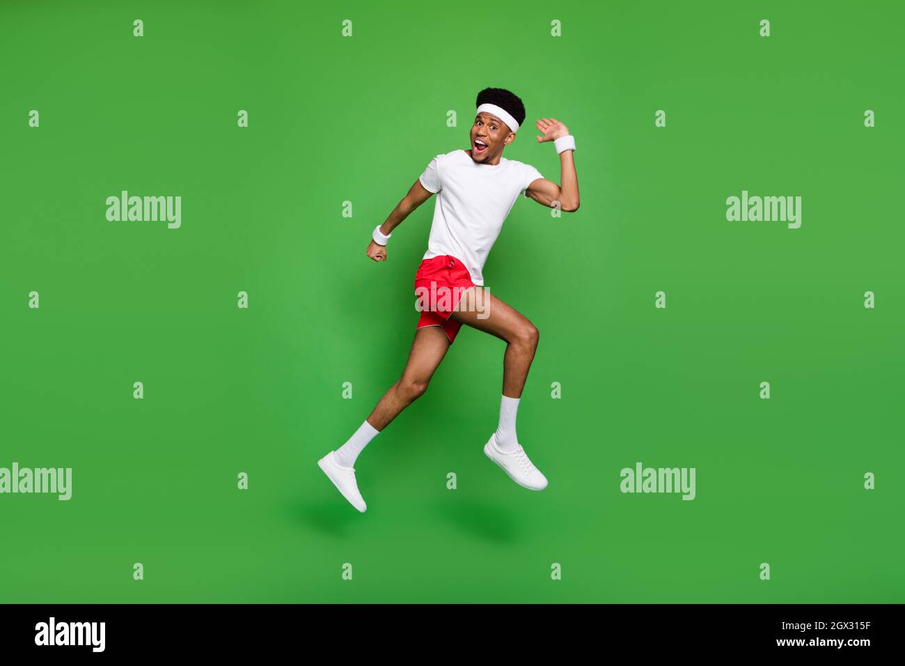 Full length photo of excited funny dark skin man wear white t-shirt jumping  high running fast isolated green color background Stock Photo - Alamy