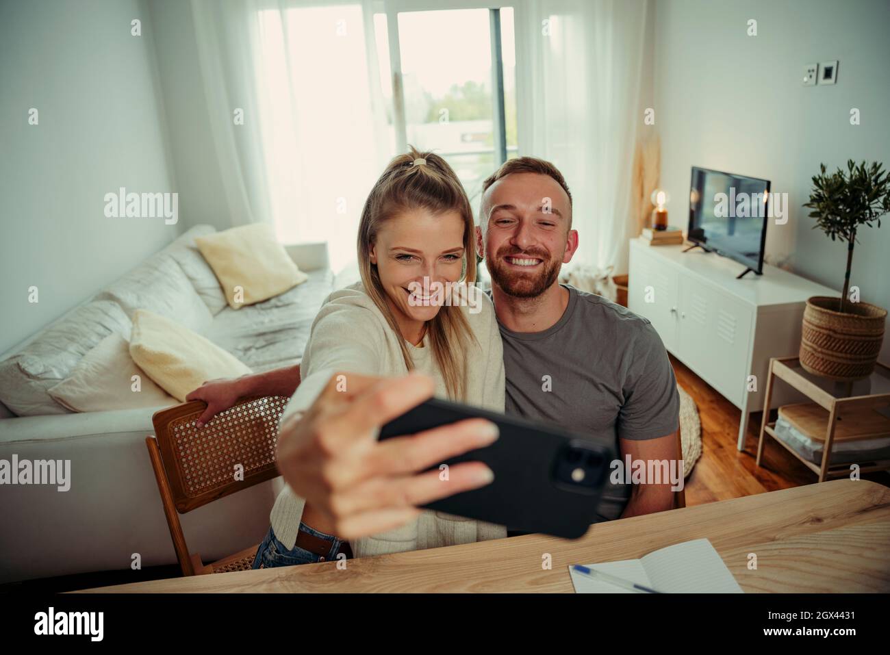 Caucasian couple taking selfie at kitchen table with cellular device Stock Photo