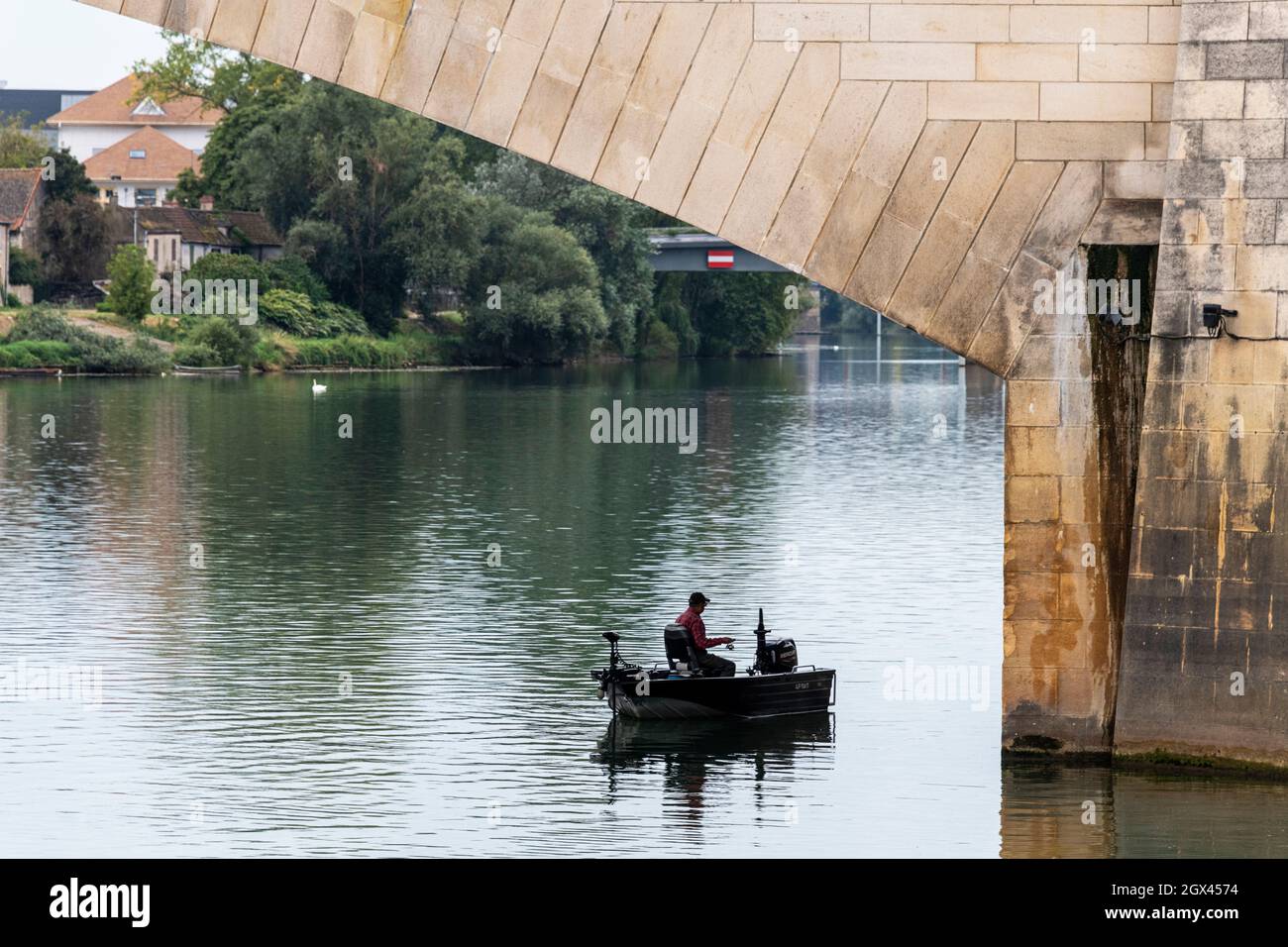 A fisherman in his boat line fishing on the River Saone, under the Saint Laurent Bridge in Chalon Sur Saone, France. Stock Photo