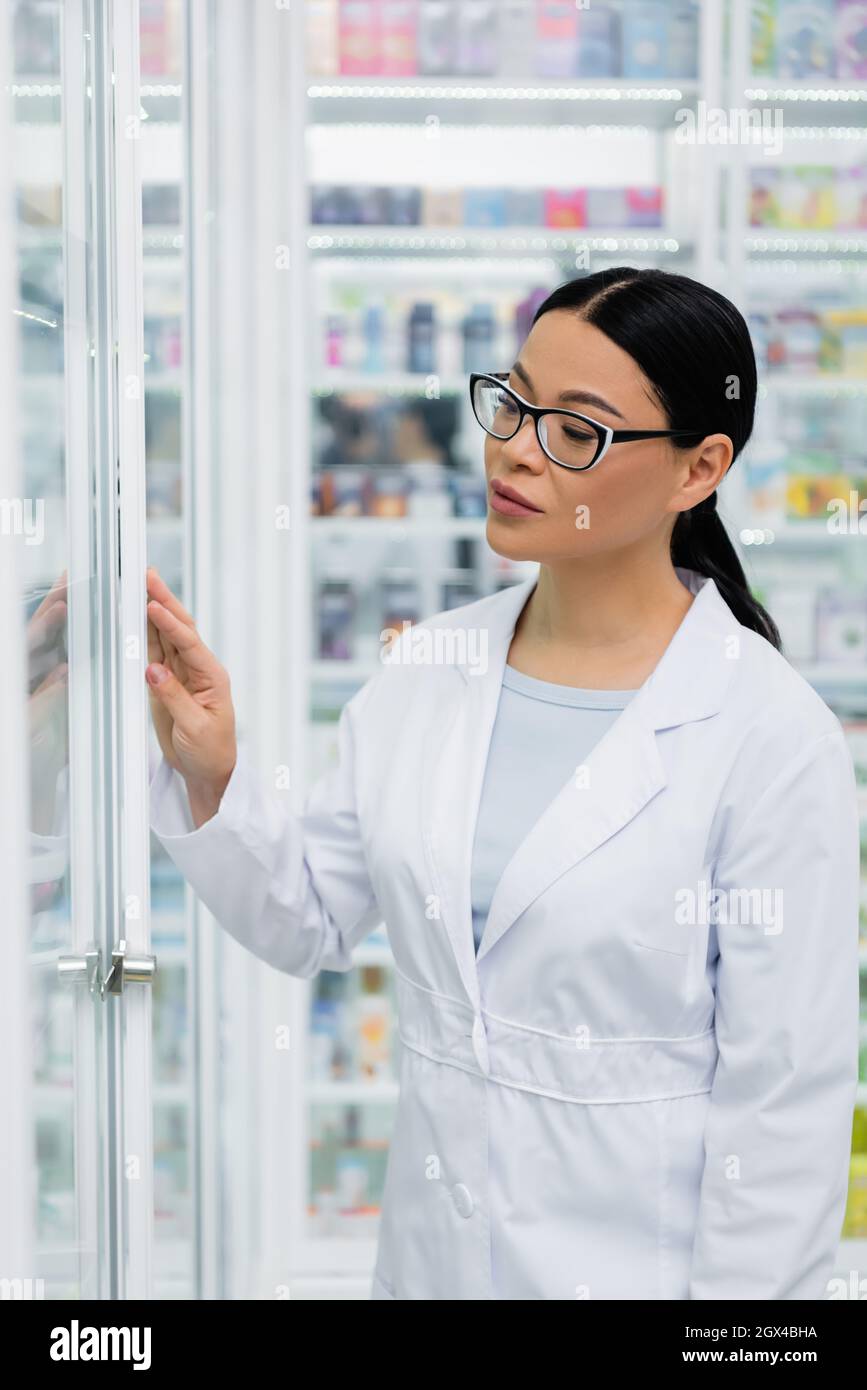 asian pharmacist in glasses looking at medication on blurred shelves Stock Photo