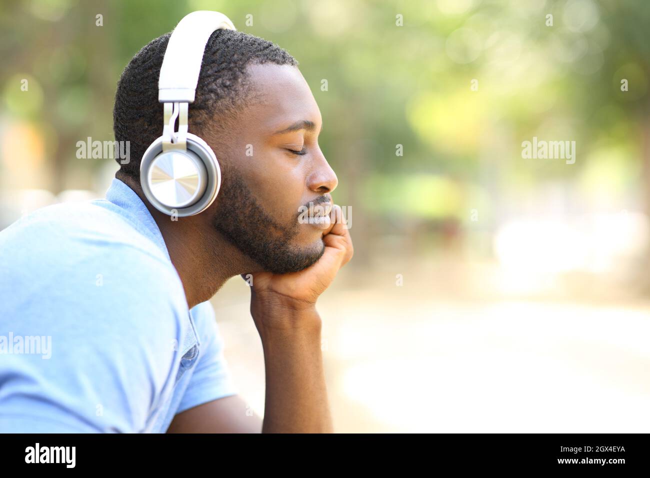 Profile of black man listening to music wearing wireless headphones in a  park Stock Photo - Alamy