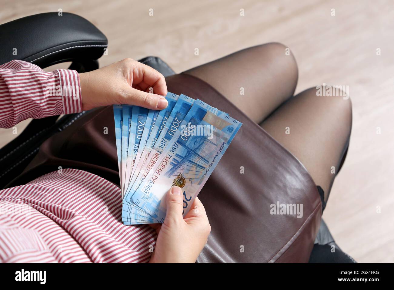 Russian rubles in female hands, cash pay, salary or bribe concept. Woman in office clothes sitting in chair with paper currency of Russia Stock Photo