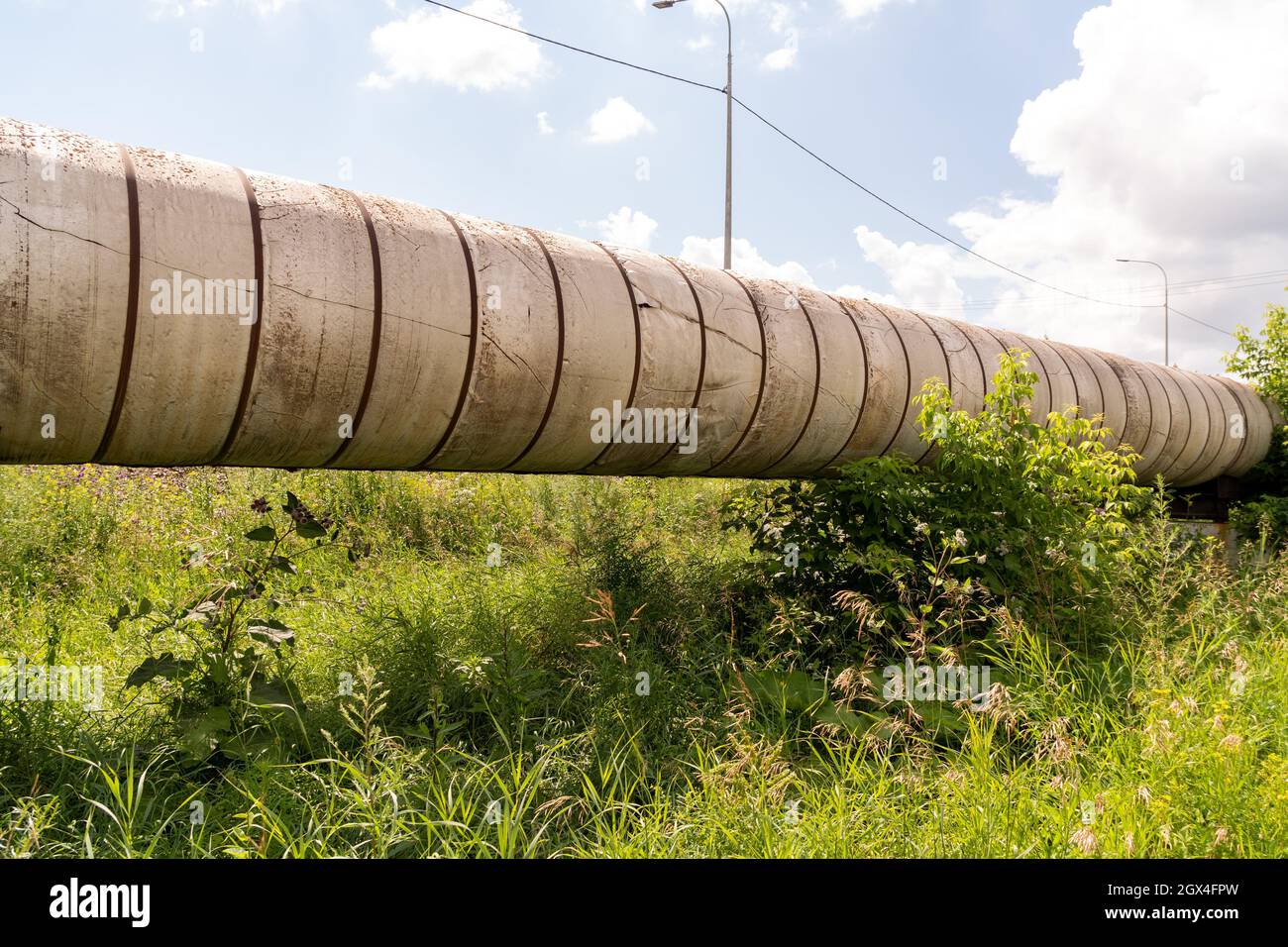 The ground pipeline of the city heating main of the main heating network on a reinforced concrete support among the grass on a sunny summer day. Stock Photo