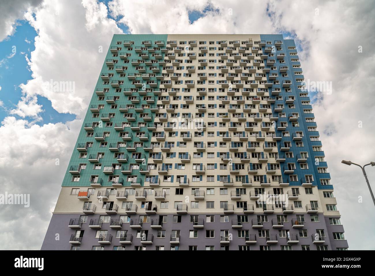 The facade of a multi-apartment new residential building with balconies and windows, painted in 4 colors against a cloudy sky. Stock Photo