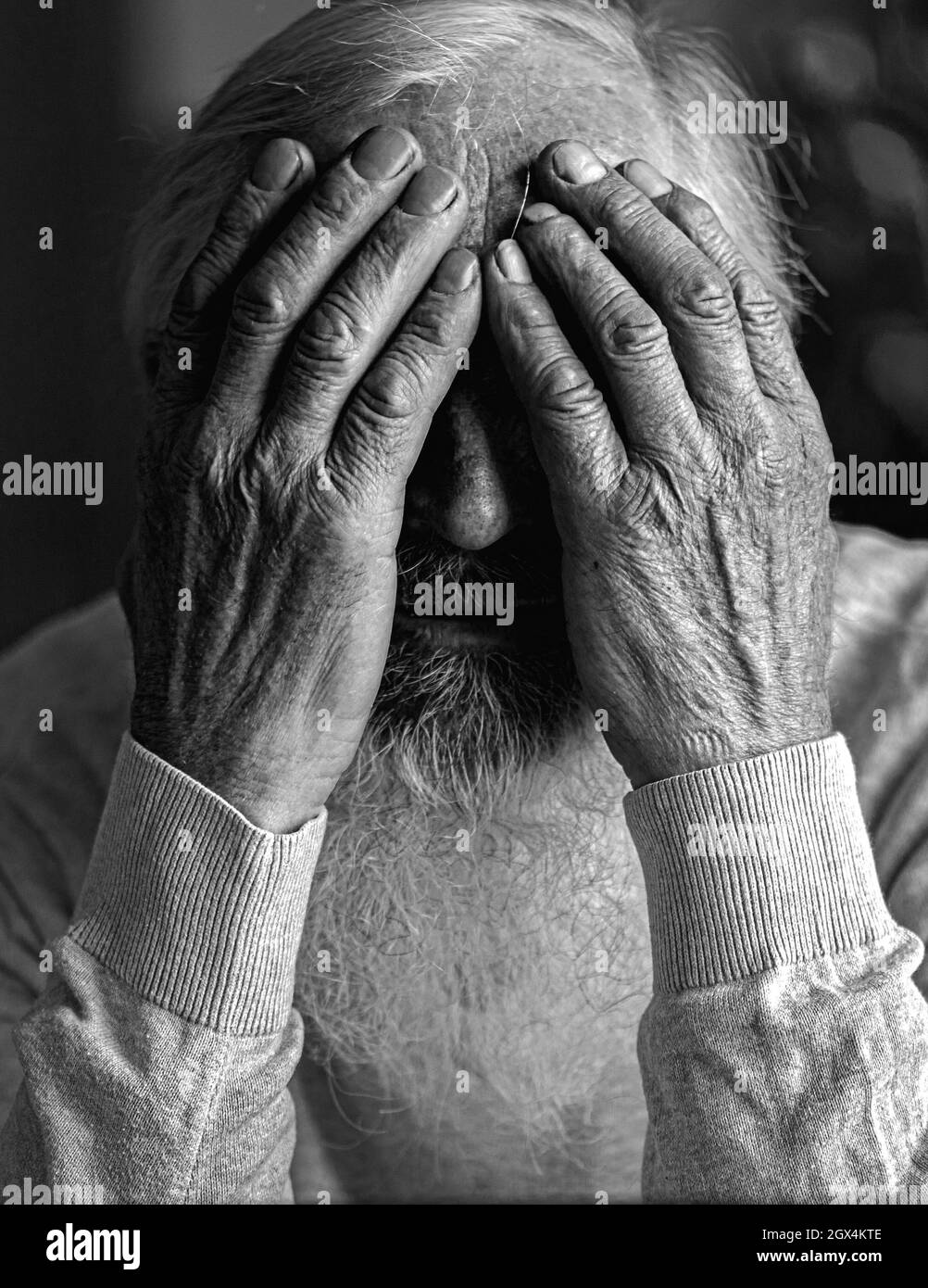 A tired, broken, resigned, preoccupied elderly man sits in front of a laptop, computer and covers his face with his hand. Stock Photo