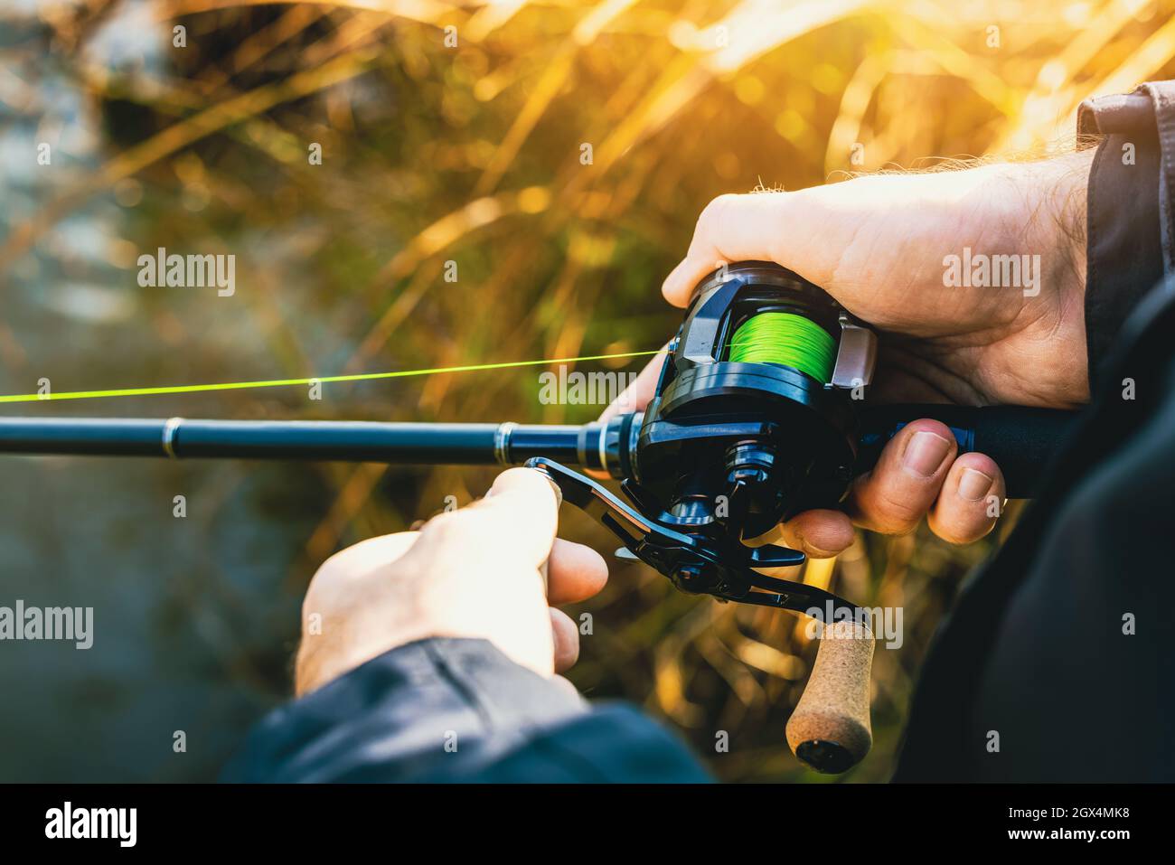 fishing rod with multiplier reel and green braided line in angler hands. closeup Stock Photo