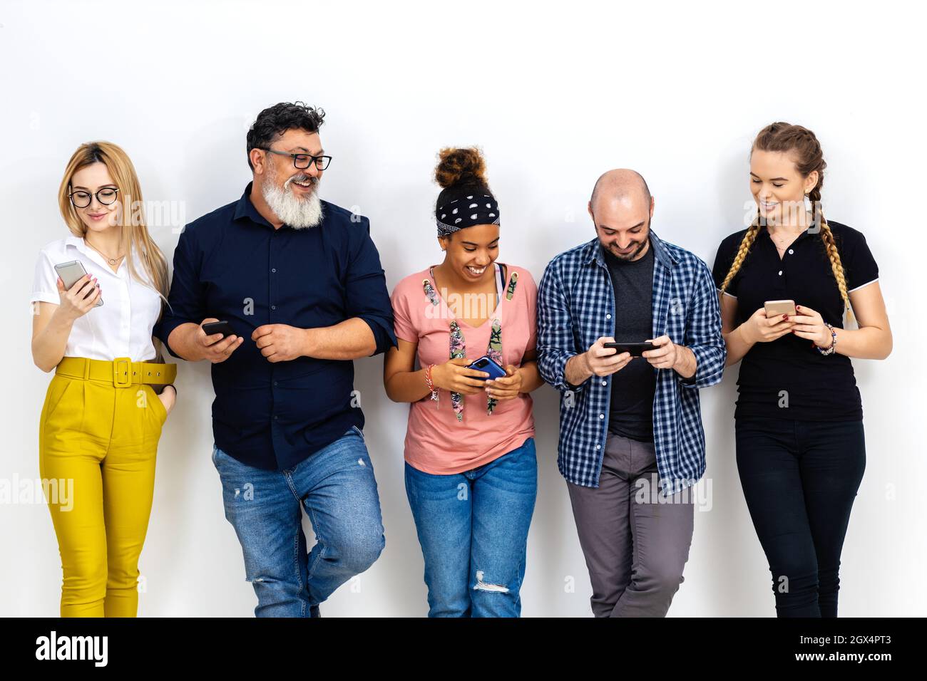 Multiracial friends laughing while using mobile phones against wall Stock Photo