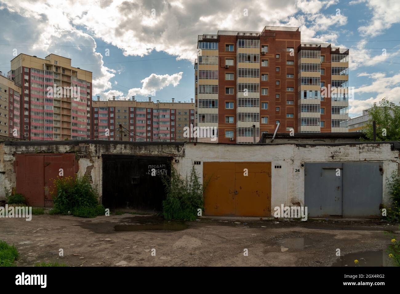 Garages are in a row in a residential area on a summer day, one of them has an inscription in Russian - sell. Stock Photo
