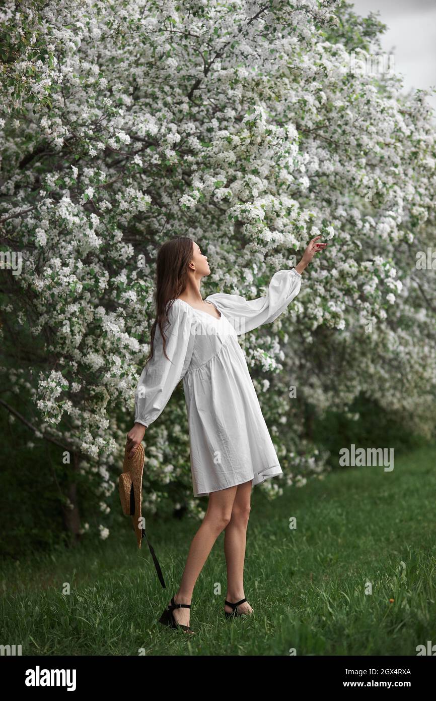 Young woman in white dress with a straw hat walks through blooming ...