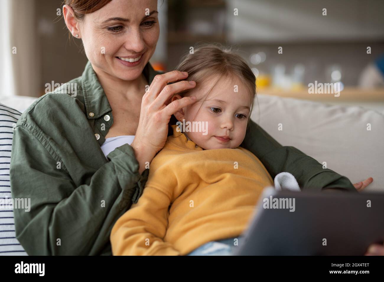 Happy mother with small daughter watching kids programme on tablet indoors at home, single parenting concept. Stock Photo