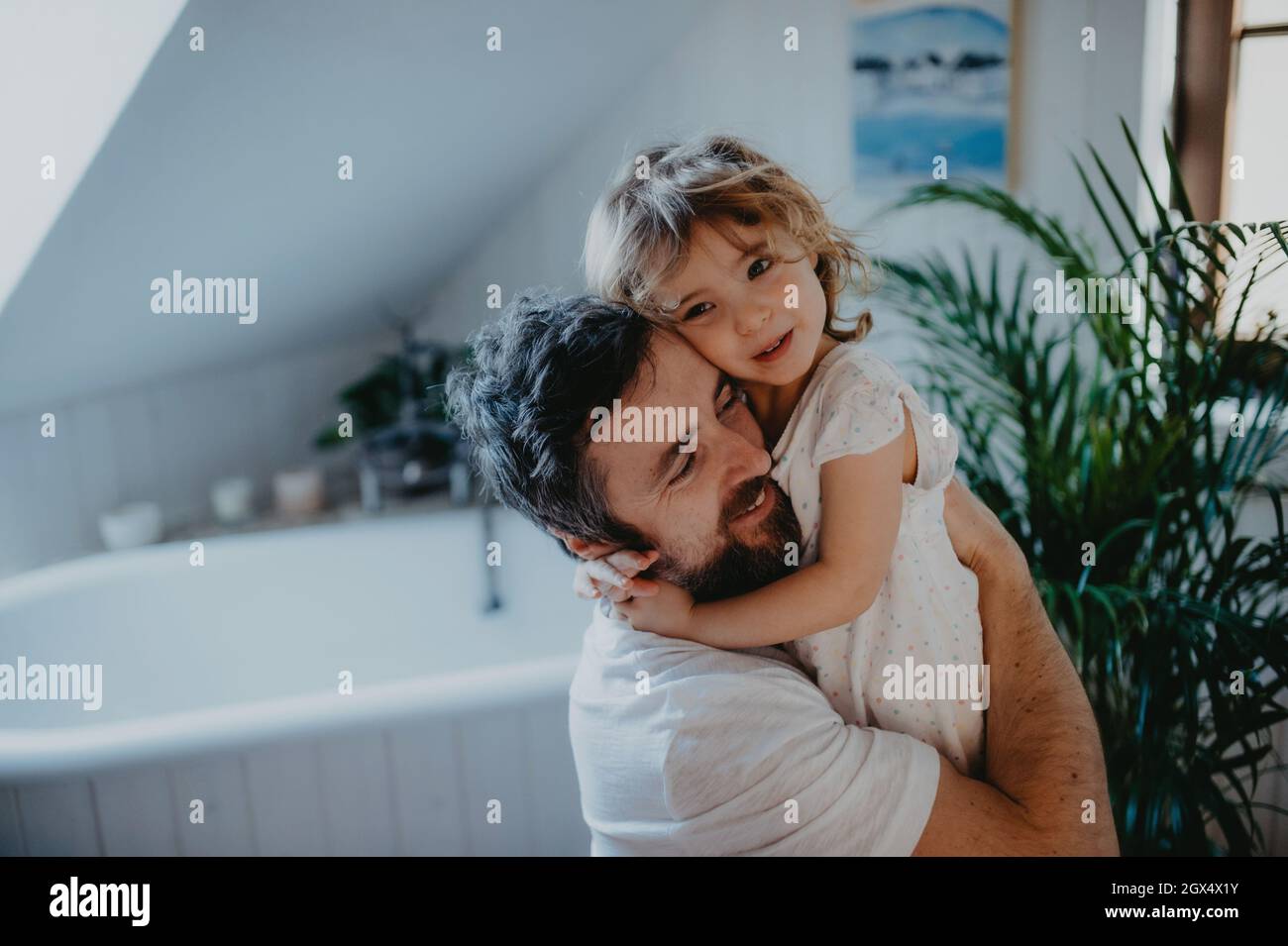 Mature father hugging with small daughter indoors in bathroom at home. Stock Photo