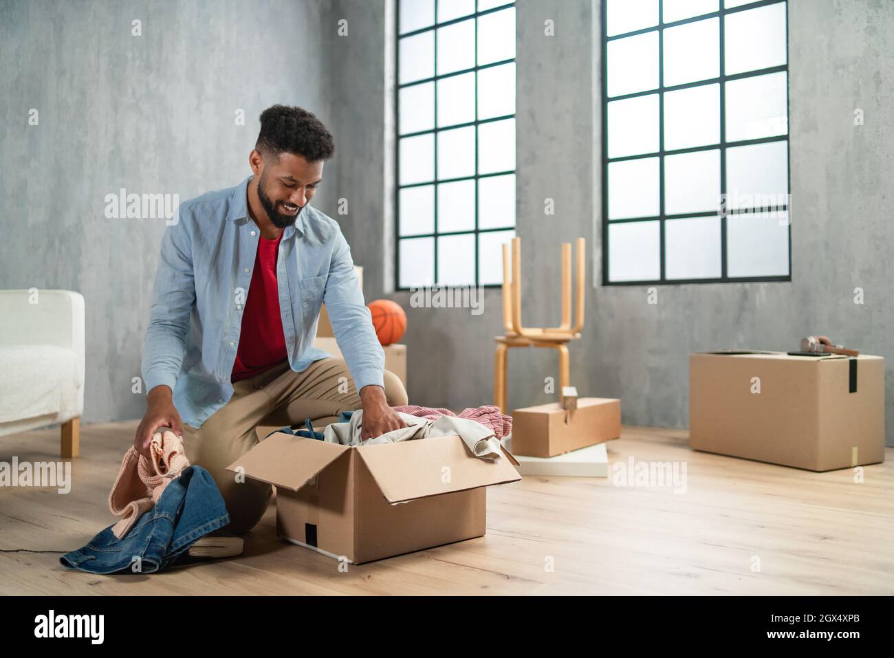 Happy young man putting clothes into packing boxes, moving home. new