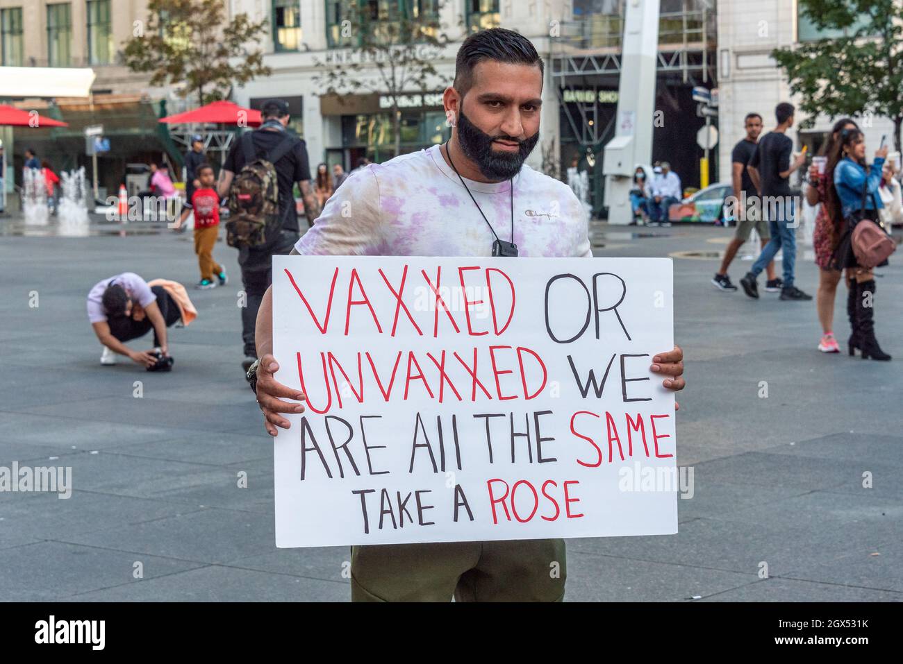 A man with a sign reading 'Vaxxed or Unvaxxed We Are All The Same, Take a Rose'. He is seen in the Yonge-Dundas Square in Toronto city, Canada Stock Photo