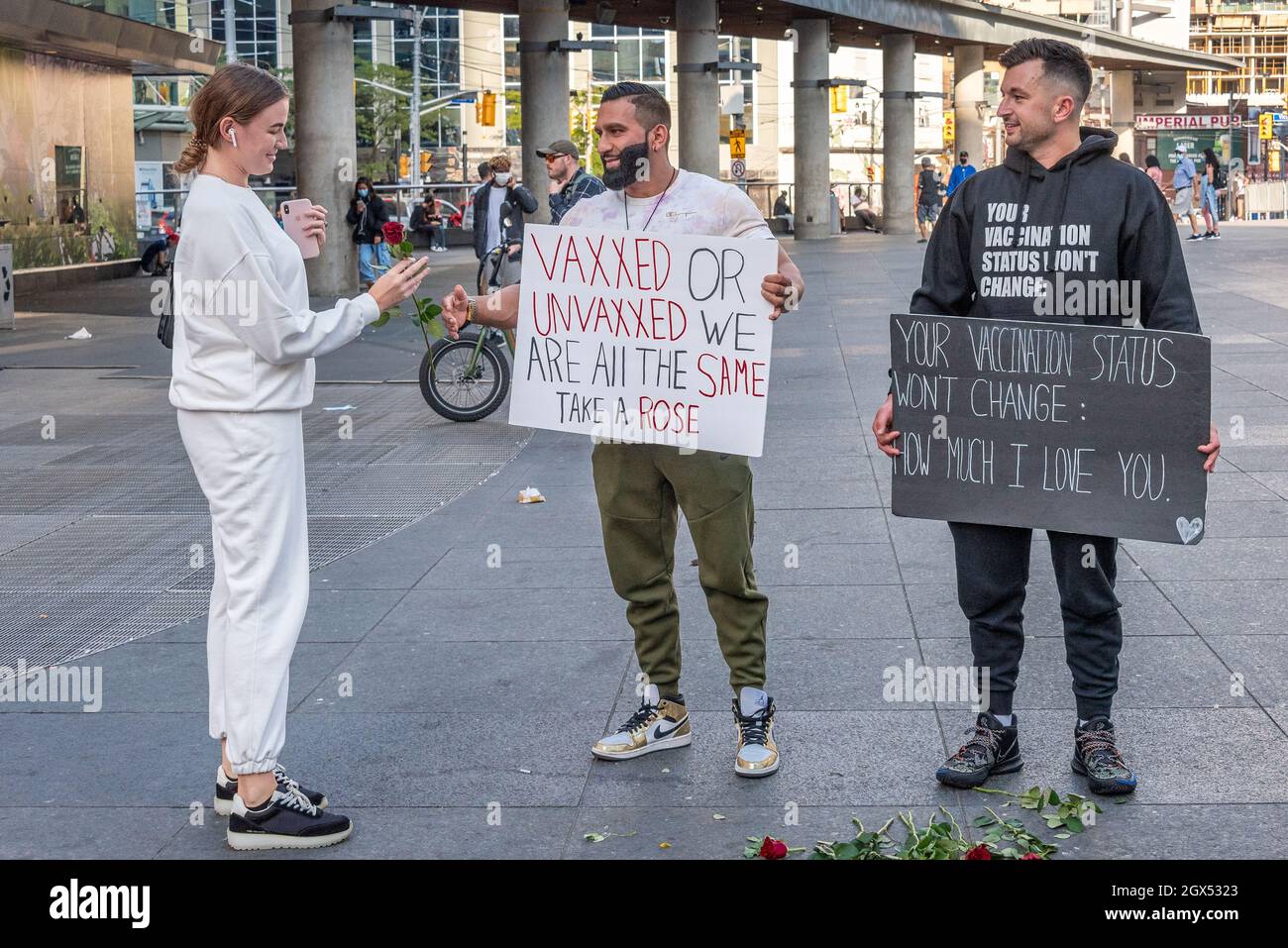 Two men giving away roses in Yonge-Dundas Square in Toronto city, Canada. They have a sign reading 'Vaxxed or Unvaxxed We Are All The Same, Take a Ros Stock Photo