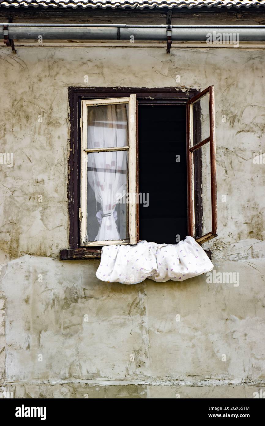 A duvet in the open window of the house with rough plaster without paint Stock Photo