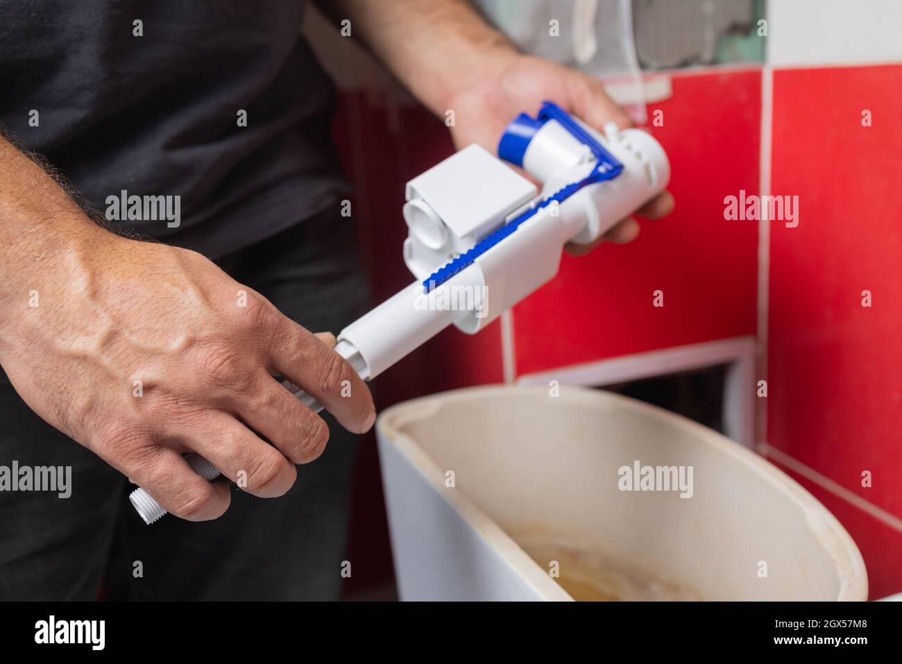 Toilet tank parts replacement. A man in orange gloves repairs the toilet tank drain Stock Photo