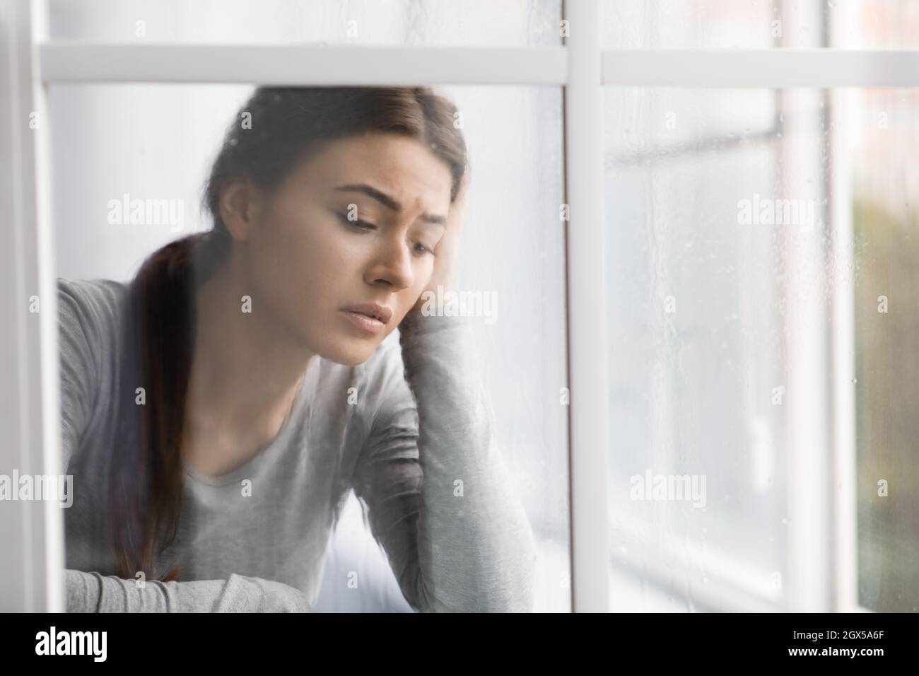 Sad anxiety unhappy caucasian millennial woman suffering from depression and stress and looking out the window at home Stock Photo
