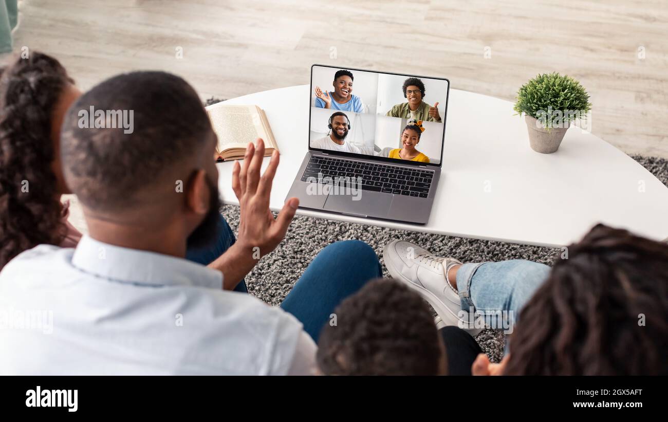 Millennial black husband and wife with children look at laptop screen ...