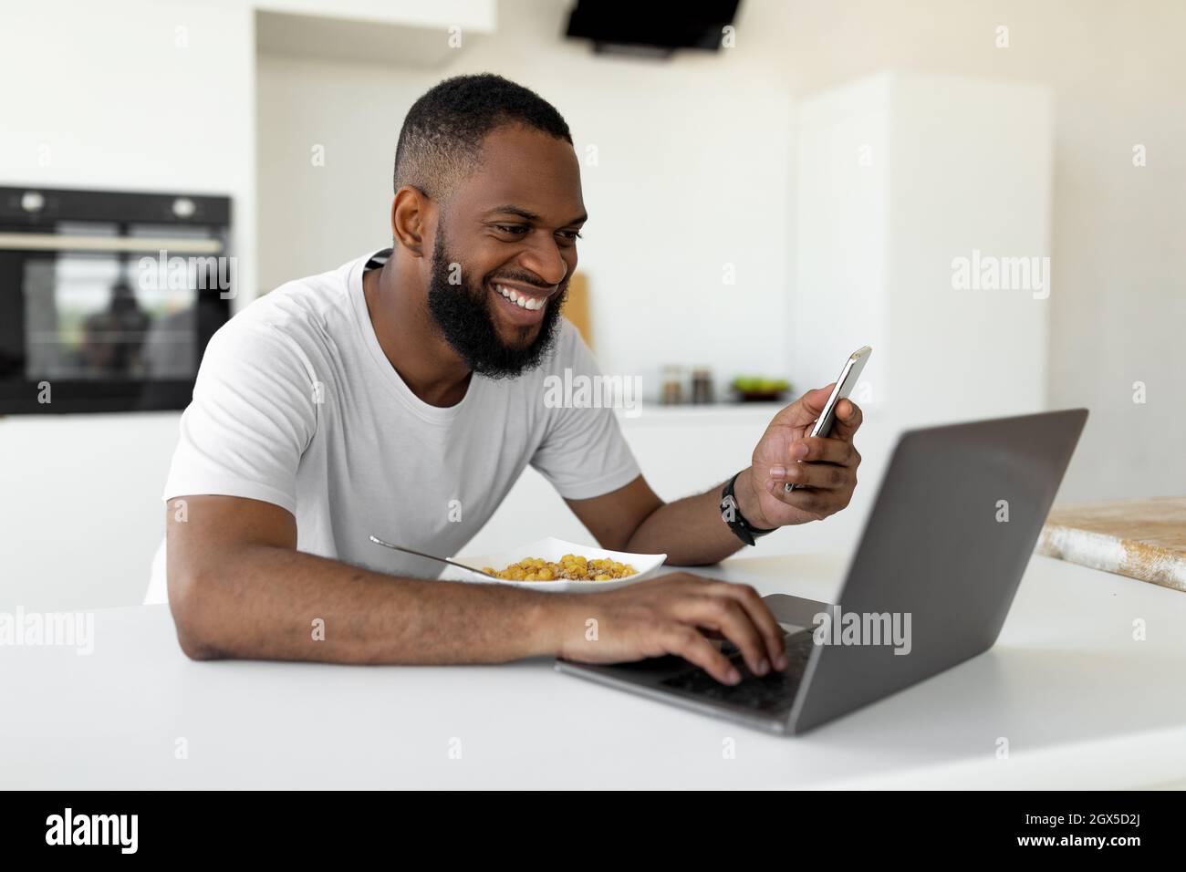 Black man using pc and smartphone having breakfast at home Stock Photo