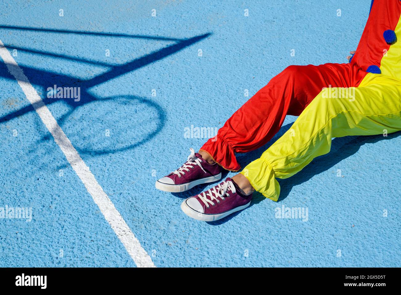 closeup of a man, wearing a colorful clown costume, sitting an outdoor basketball court Stock Photo