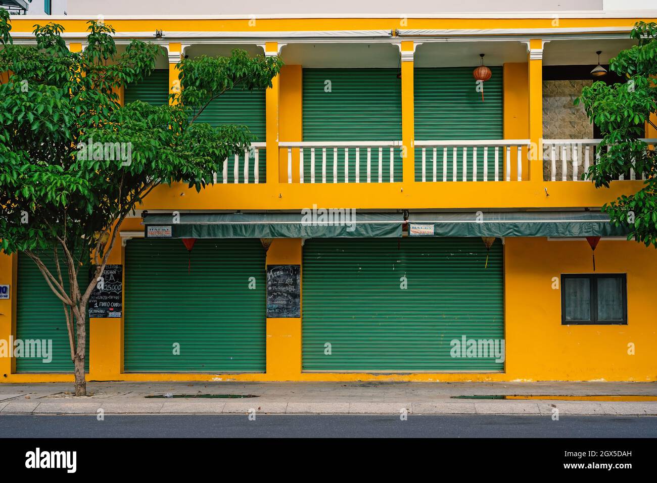 Bright yellow building facade with green roller shutters, front view. Asian architecture, colonial style.  Nha Trang, Vietnam: 2020-10-23 Stock Photo