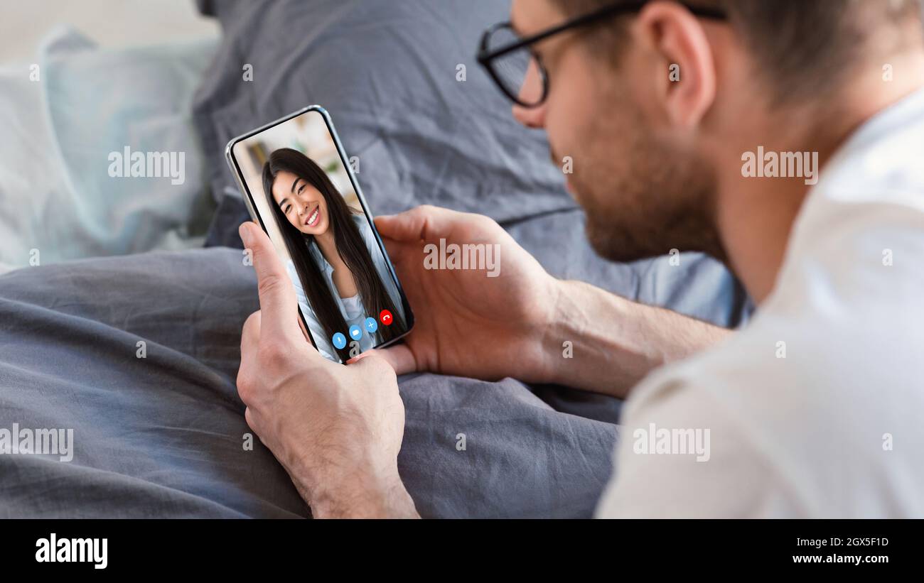 Young man using smartphone for web chat with his asian girlfriend Stock Photo