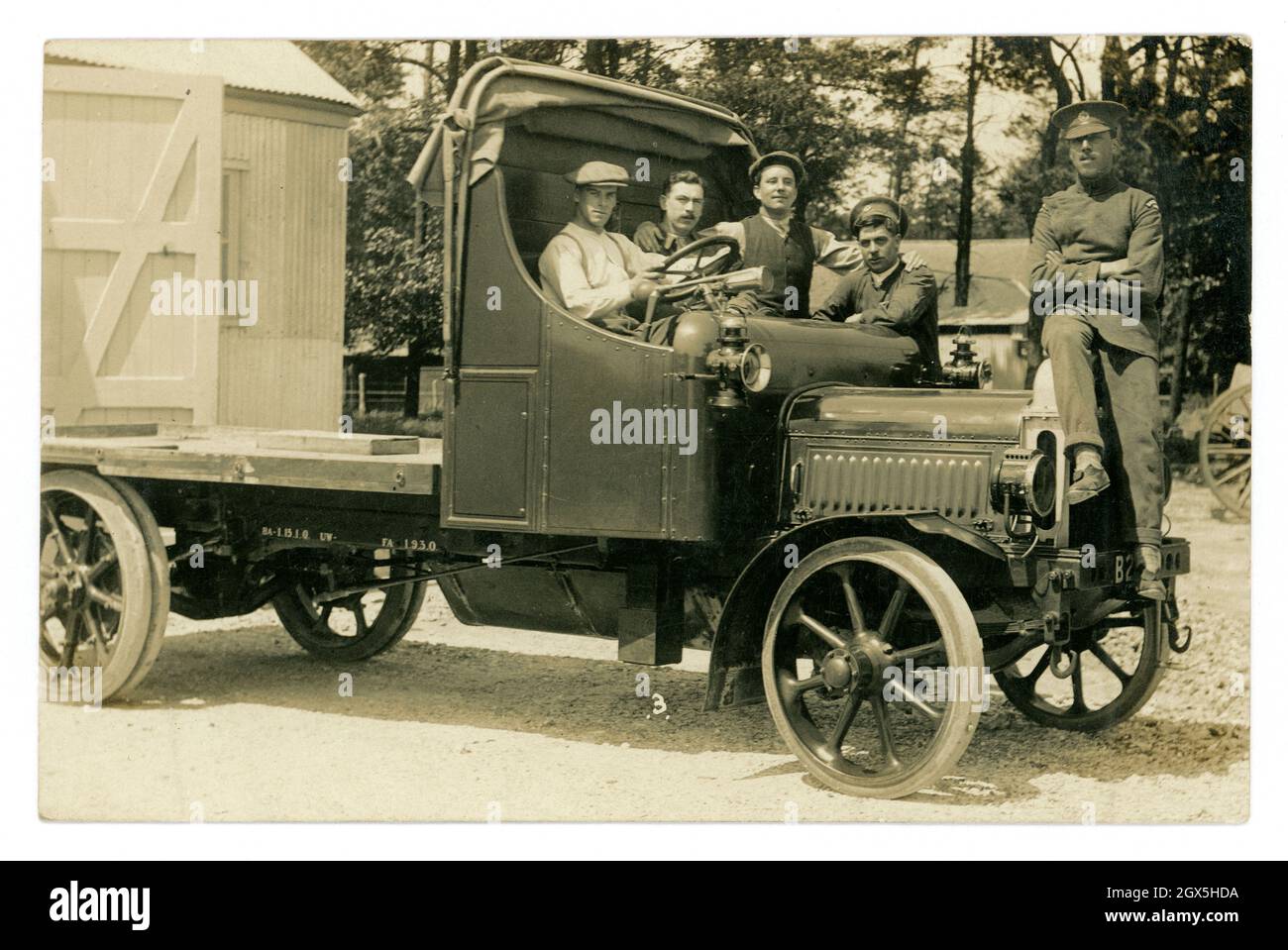 Original very clear WW1 era postcard of group young men from the Royal Flying Corps in a flatbed truck which was registered in Lancashire. Some of the men are in uniform with the RFC badge on their caps. On an army base with a hut or hangar, the wheels of a field gun can just be seen, perhaps these men were transporting artillery. circa 1917, U.K. Stock Photo