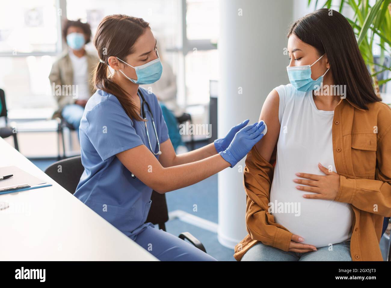 Pregnant Asian Woman Preparing To Get Vaccinated, Doctor Disinfecting Arm Stock Photo