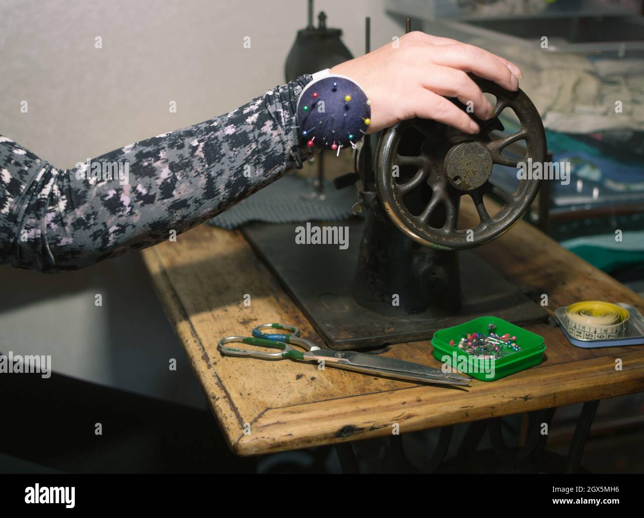 Female hand in spotted clothes turns flywheel of old sewing machine