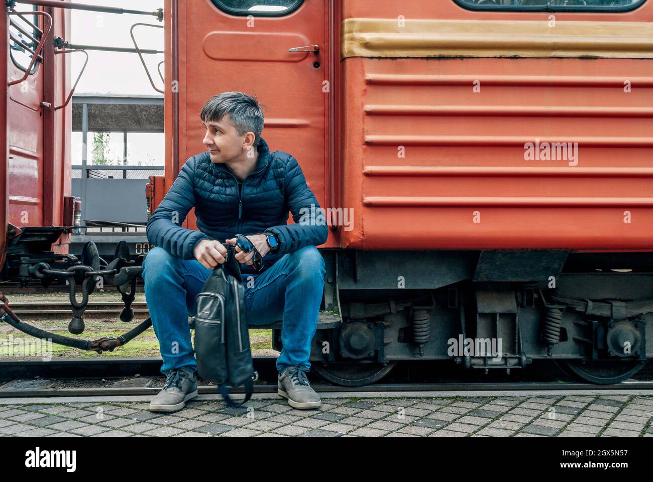 A man sitting on the background of an old train looks to the left Stock Photo