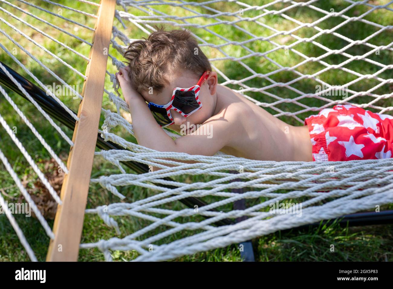 Young boy relaxing on his stomach in a hammock wearing sunglasses Stock