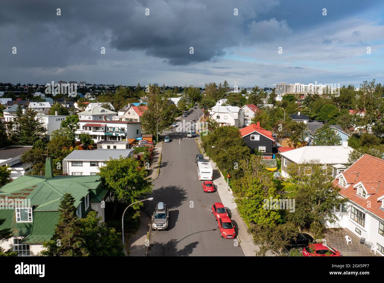 Aerial view of modern vehicles driving on asphalt road near suburban cottages and green trees on overcast day in town. Stock Photo