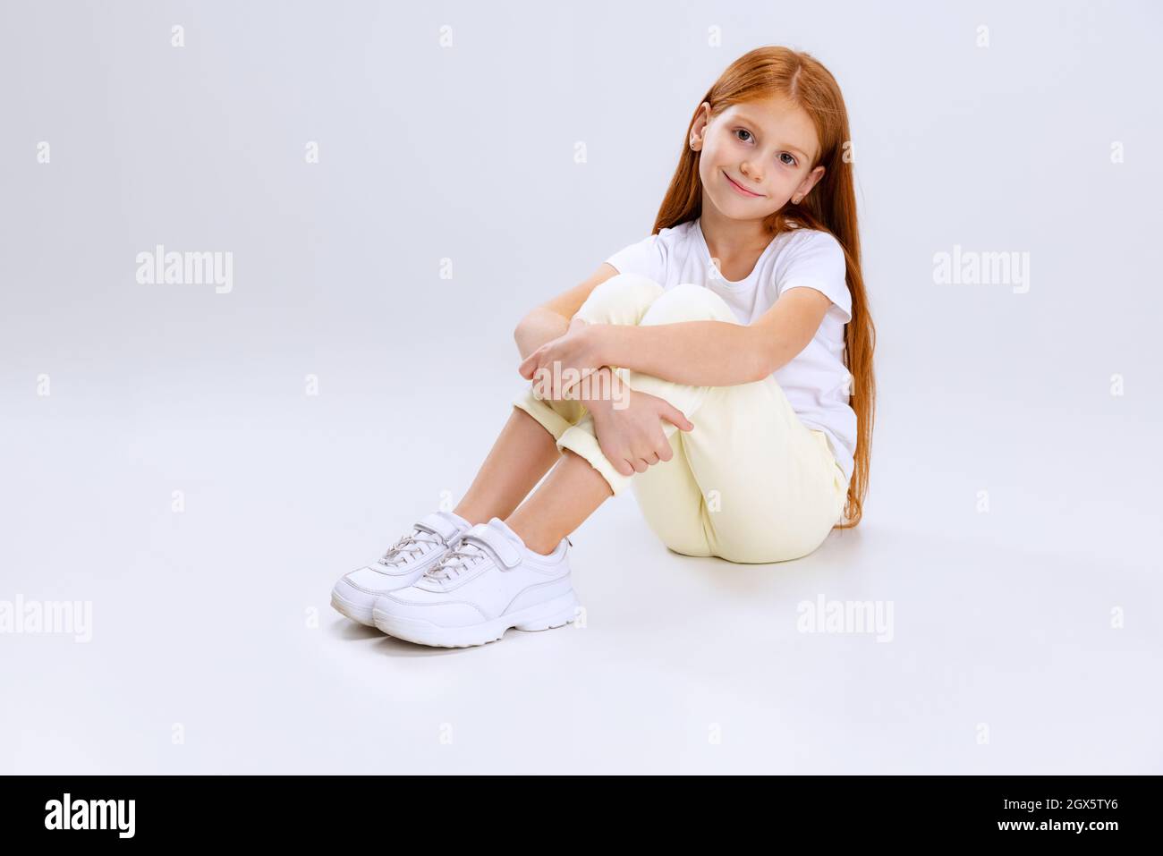 Portrait of little Caucasian cute girl calmly sitting and smiling isolated over gray studio