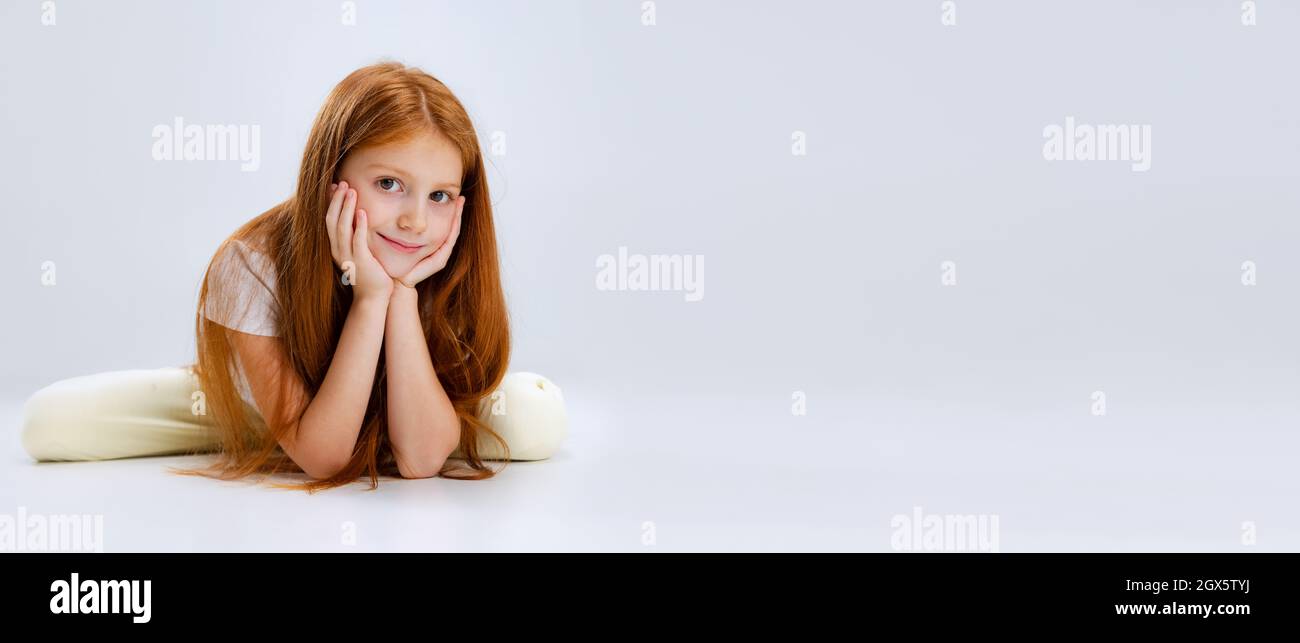 Portrait of little Caucasian cute girl calmly lying on floor and propping cheecks with hands