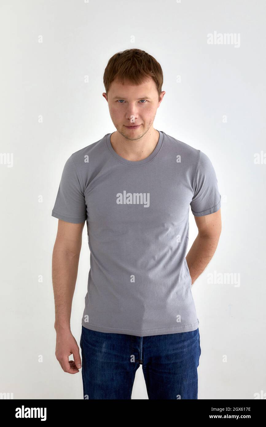 Positive young male in jeans hand behind and gray t shirt standing against white background and looking at camera Stock Photo