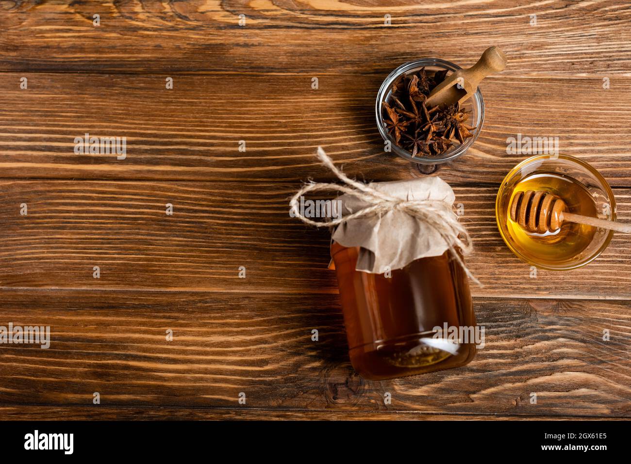 top view of honey jar covered with craft paper near bowls with anise seeds, scoop and dipper on wooden table Stock Photo