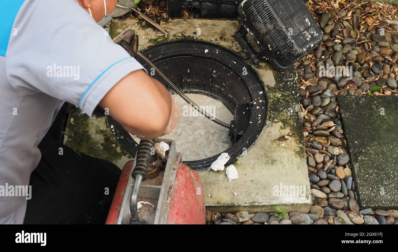 Drain cleaning. Plumber repairing clogged grease trap with auger