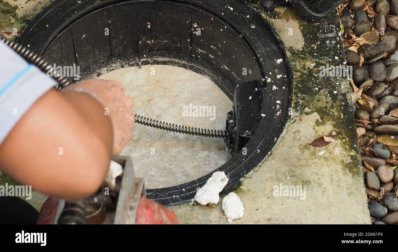 Drain cleaning. Plumber repairing clogged grease trap with auger