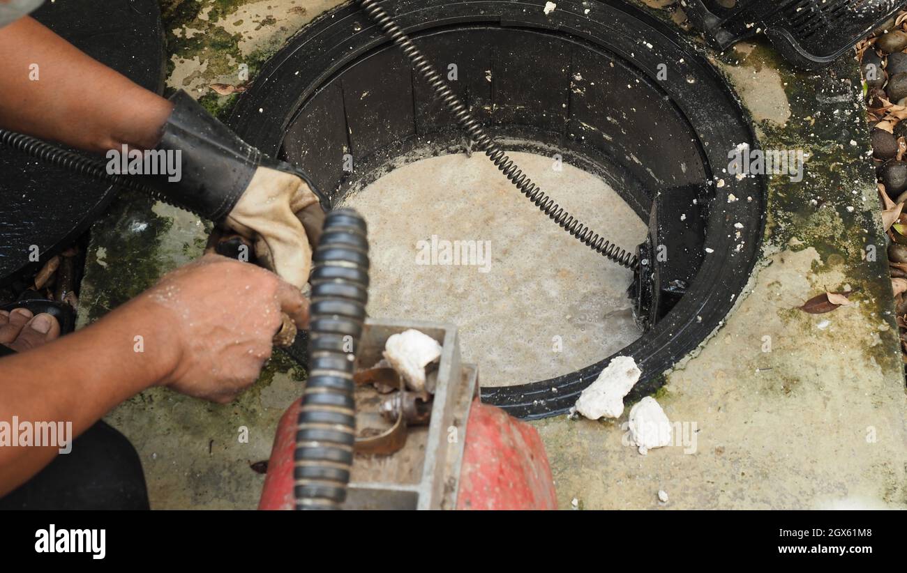 Drain cleaning. Plumber repairing clogged grease trap with auger