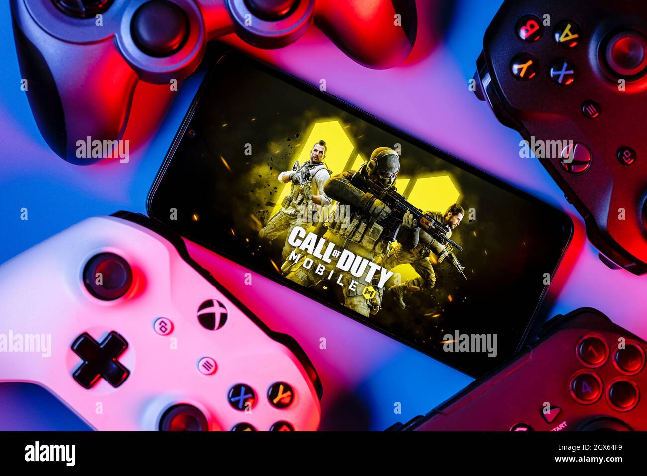 A smartphone with the frame from Call of Duty on the screen surrounded by gamepads. Stock Photo