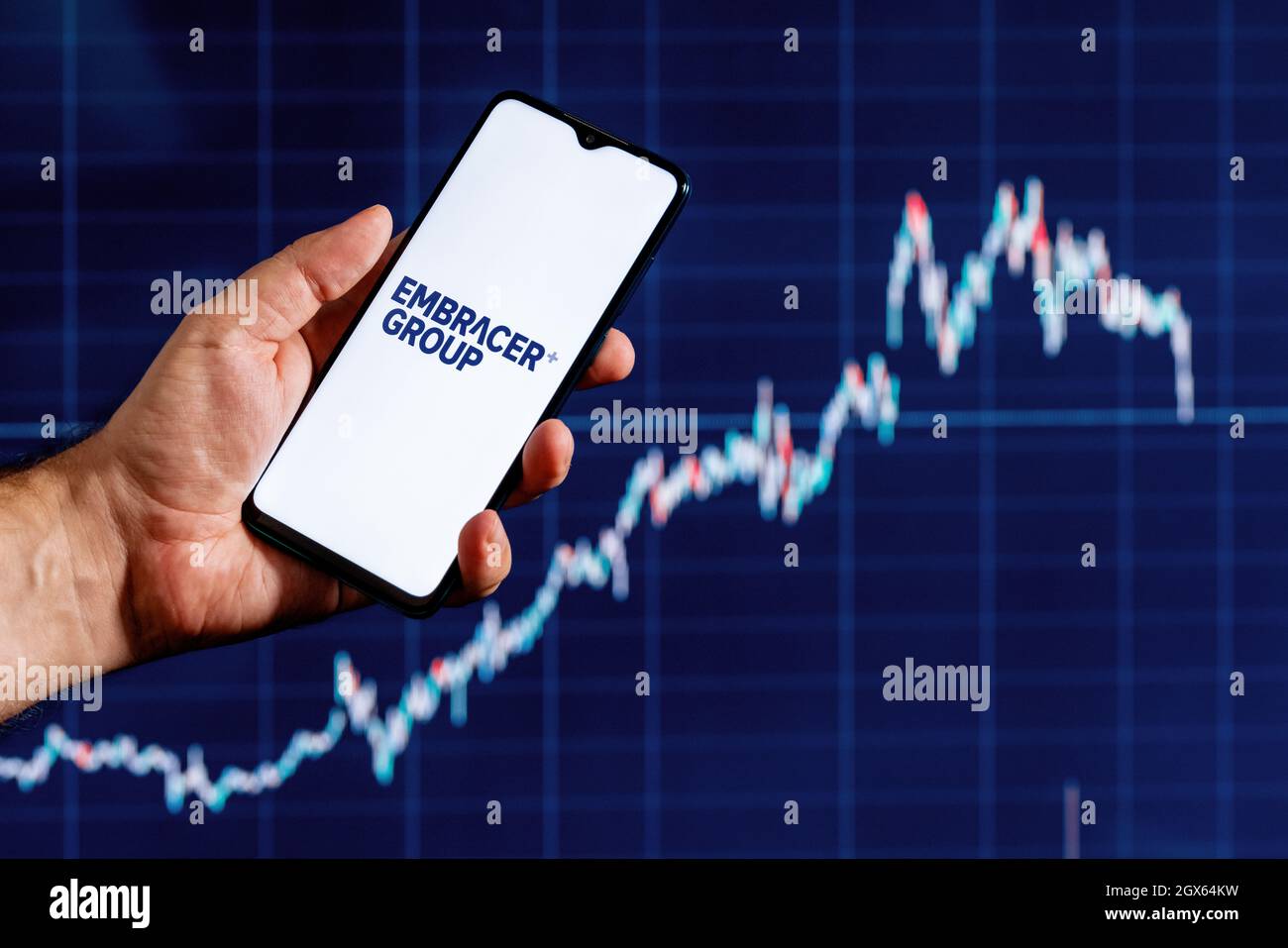A smartphone with the Embracer Group logo in a hand. Stock chart on the background. Stock Photo