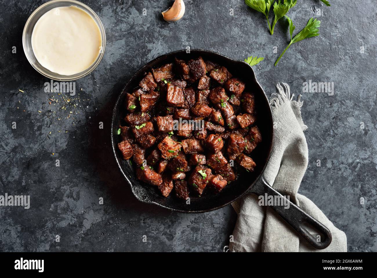 Garlic butter steak bites in cast iron pan over stone background. Top