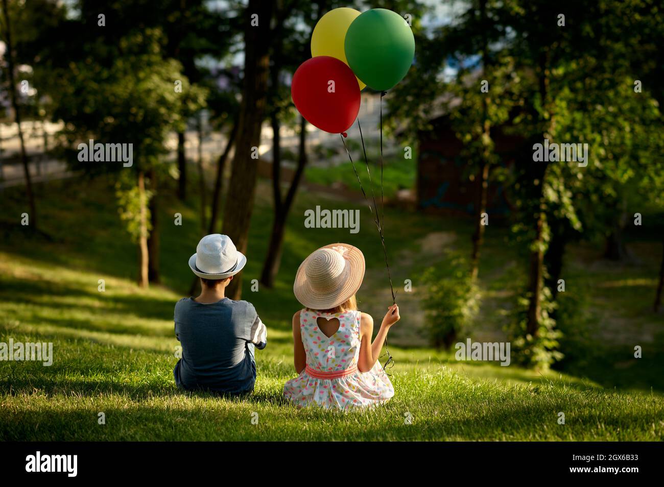 Boy and girl with air balloons sitting on a grass Stock Photo - Alamy