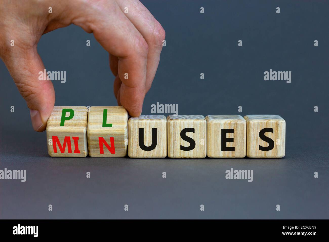 Pluses and minuses symbol. Businessman turns wooden cubes and changes the word 'minuses' to 'pluses'. Beautiful grey table, grey background. Business, Stock Photo